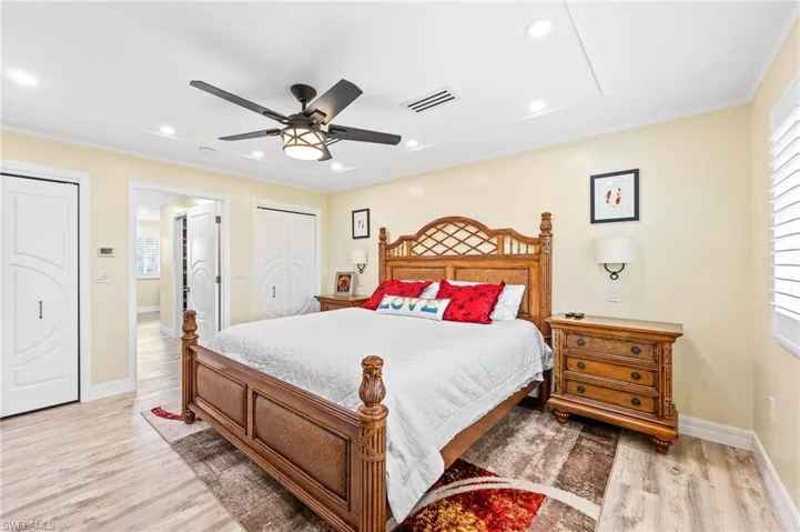 Spacious Master Bedroom featuring light wood finished floors, a ceiling fan, recessed lighting, crown molding, and multiple closets