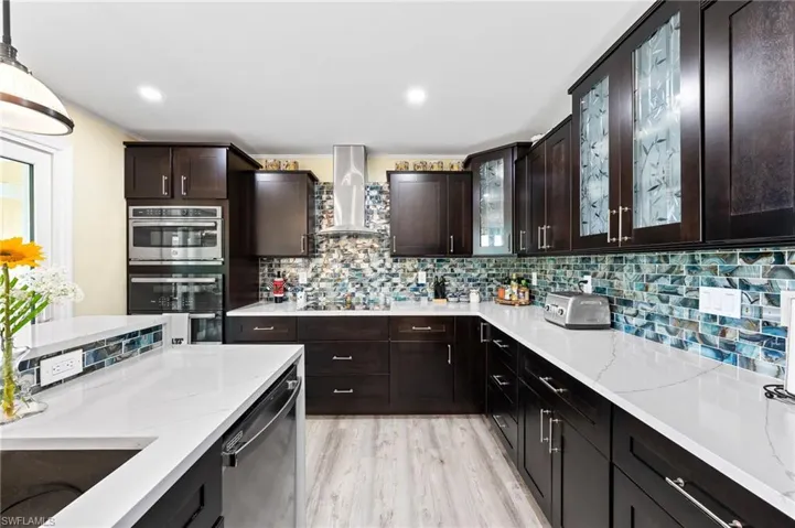 Kitchen with light stone counters, decorative backsplash, dark brown cabinets, high-volume kitchen exhaust hood to the outside, stainless steel appliances