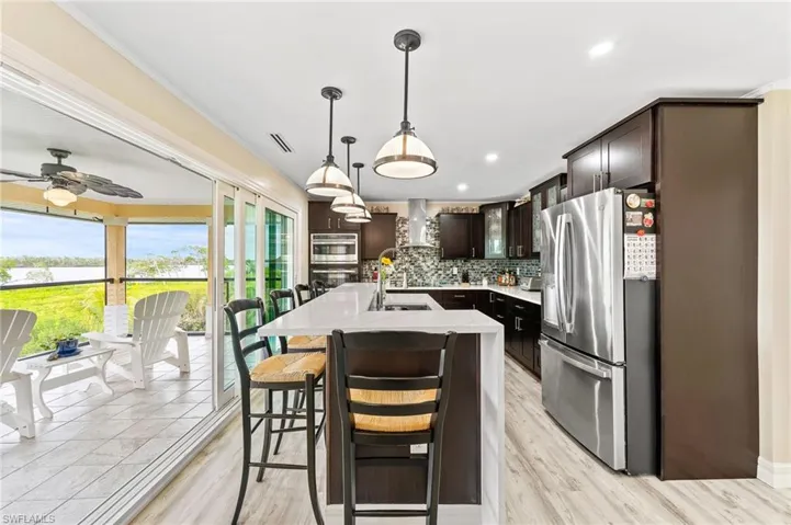 Kitchen with stainless steel refrigerator with ice dispenser, pendant lighting, glass insert cabinets, dark brown cabinets, and ornamental molding