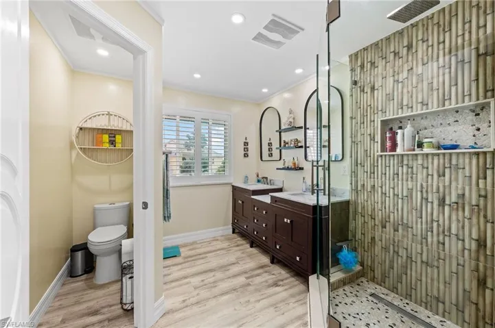 Full master bathroom with dual vanity, a shower stall with glass doors and custom bamboo-style tiles, light wood finished floors, crown molding, and recessed lighting