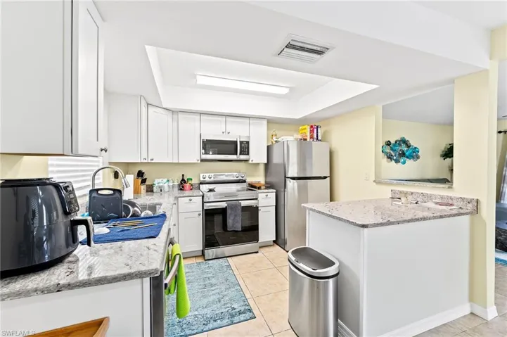 Full-size separate kitchen in the separate apartment featuring light stone counters, stainless steel appliances, light tile patterned floors, and white cabinets