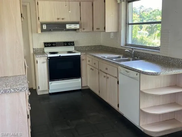 Kitchen with decorative backsplash, ventilation hood, sink, light brown cabinets, and white appliances