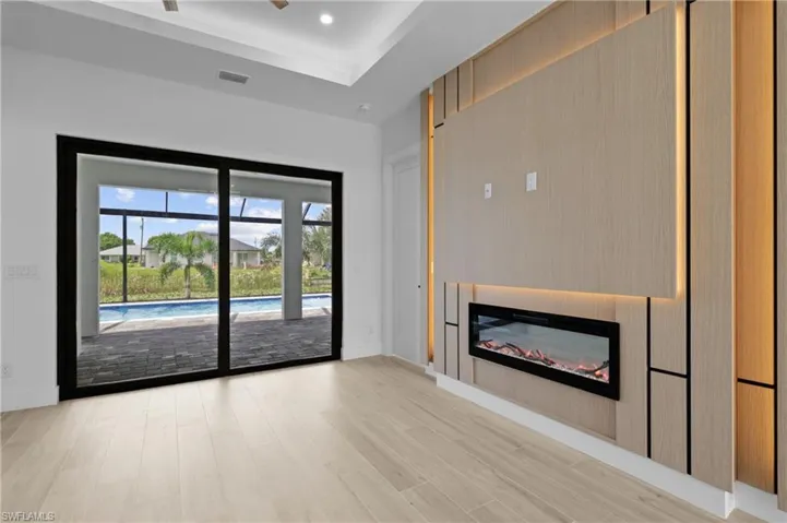 Unfurnished living room with a glass covered fireplace, light wood finished floors, recessed lighting, a ceiling fan, and a tray ceiling