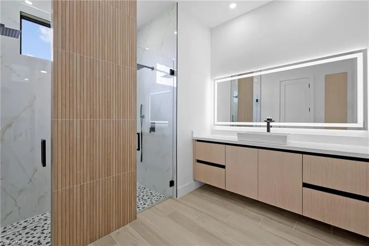 Bathroom featuring a marble finish shower, vanity, wood tiled floors, and recessed lighting
