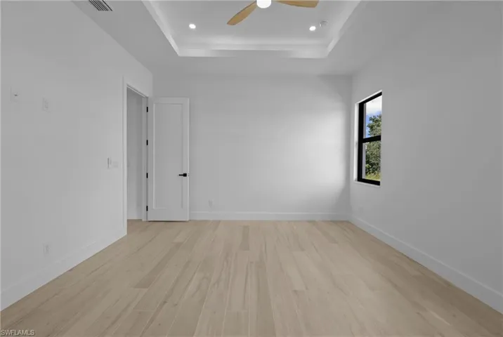 Unfurnished room featuring light wood-style flooring, a tray ceiling, recessed lighting, and a ceiling fan