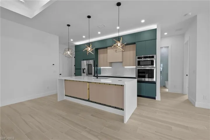 Kitchen with modern cabinets, wood finish floors, a center island with sink, decorative light fixtures, and appliances with stainless steel finishes