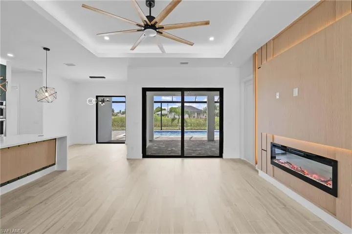Unfurnished living room featuring a raised ceiling, light wood finished floors, recessed lighting, a glass covered fireplace, and ceiling fan