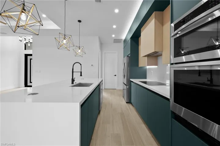 Kitchen with appliances with stainless steel finishes, modern cabinets, light wood-style floors, hanging light fixtures, and a center island with sink