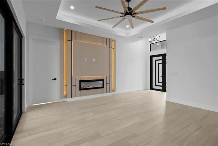 Unfurnished living room featuring recessed lighting, light wood-style floors, a raised ceiling, a glass covered fireplace, and ceiling fan