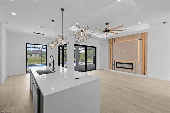 Kitchen with decorative light fixtures, a glass covered fireplace, recessed lighting, an island with sink, and light stone counters