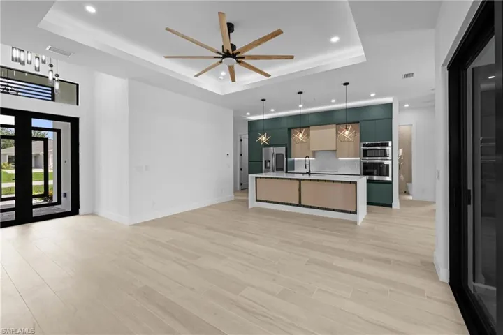 Unfurnished living room featuring a raised ceiling, recessed lighting, a ceiling fan, light wood finished floors, and french doors