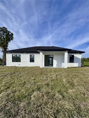 Back of house with stucco siding and a lawn