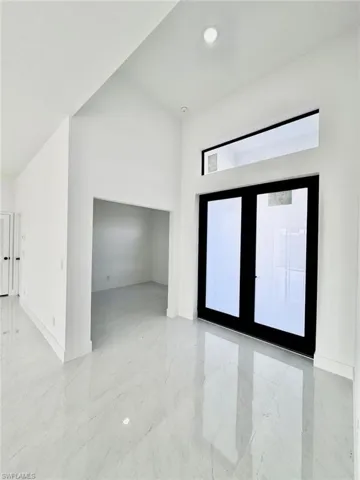 Empty room with a high ceiling, french doors, and light marble finish flooring