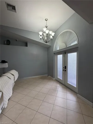 Unfurnished dining area with french doors, vaulted ceiling, light tile patterned floors, a chandelier, and a textured ceiling