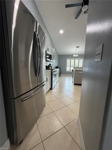 Kitchen featuring appliances with stainless steel finishes, white cabinetry, light tile patterned floors, vaulted ceiling, and hanging light fixtures