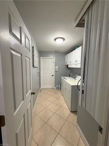 Laundry room featuring a textured ceiling, light tile patterned floors, cabinet space, and washing machine and clothes dryer