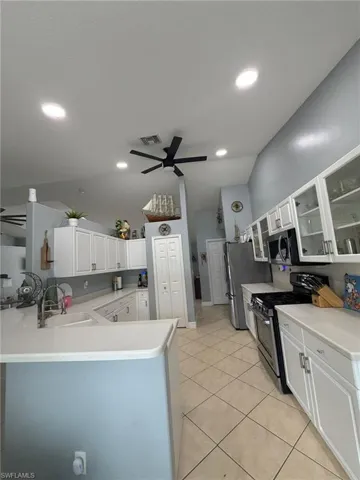 Kitchen with glass insert cabinets, stainless steel appliances, light countertops, a peninsula, and vaulted ceiling
