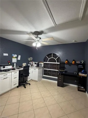 Office space featuring a textured wall, a textured ceiling, built in desk, light tile patterned floors, and a ceiling fan