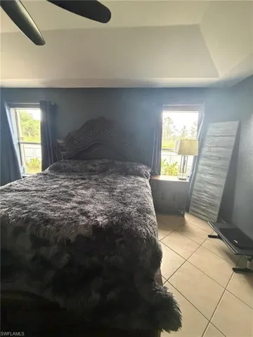 Bedroom with light tile patterned floors, multiple windows, and a ceiling fan