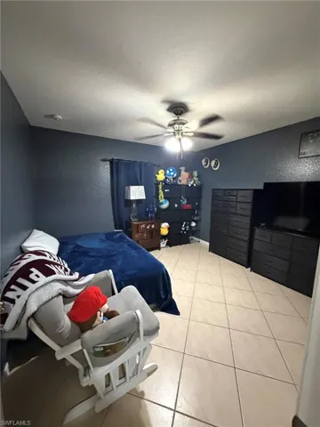 Bedroom with a textured wall, light tile patterned flooring, a textured ceiling, and ceiling fan