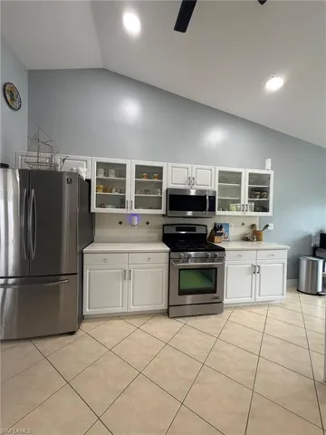 Kitchen with vaulted ceiling, white cabinets, tasteful backsplash, stainless steel appliances, and glass insert cabinets