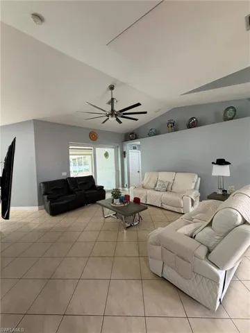 Living area featuring light tile patterned floors, vaulted ceiling, and a ceiling fan