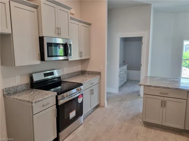 Kitchen with appliances with stainless steel finishes, light stone countertops, light wood finished floors, and baseboards