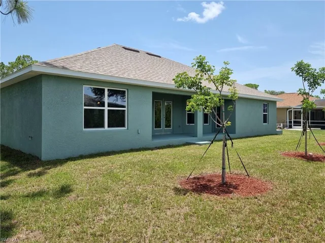 Back of house featuring stucco siding, roof with shingles, and a lawn