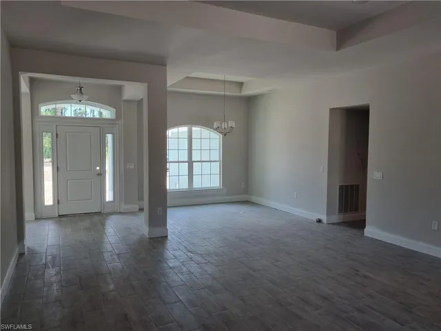 Foyer with a chandelier, baseboards, a raised ceiling, and dark wood-type flooring