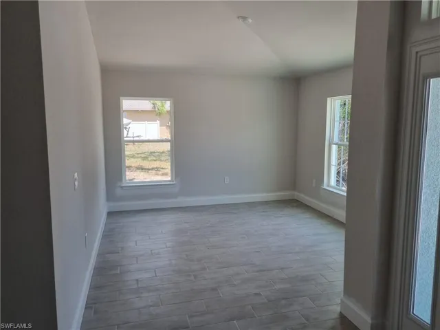 Empty room with plenty of natural light, baseboards, vaulted ceiling, and dark wood-style flooring