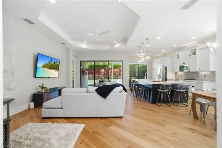 Living area with a chandelier, recessed lighting, light wood-type flooring, a ceiling fan, and a tray ceiling