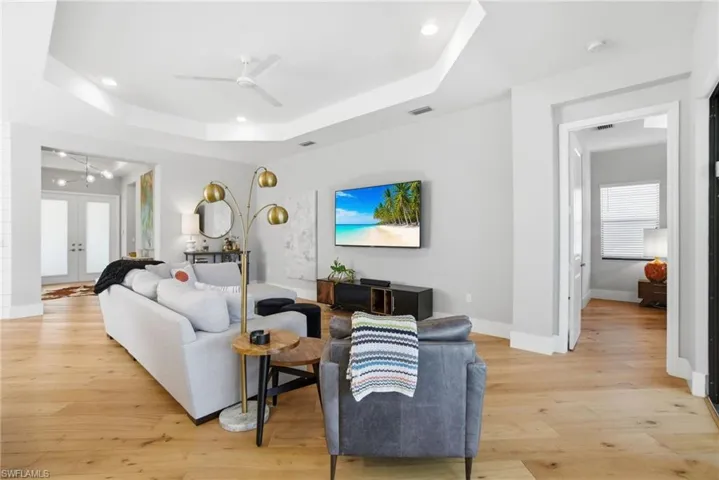 Living area featuring light wood-type flooring, ceiling fan, recessed lighting, french doors, and a tray ceiling