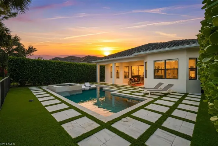 Back of house at dusk featuring a patio area, stucco siding, a fenced backyard, a tile roof, and a pool with connected hot tub