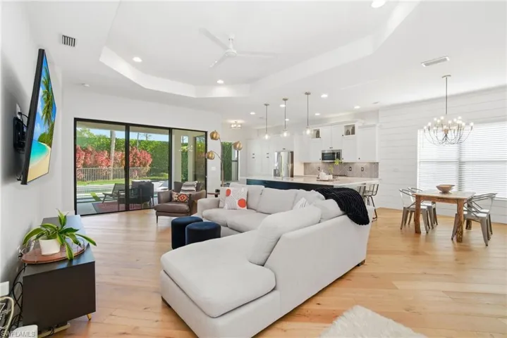 Living room with ceiling fan, light wood-style floors, recessed lighting, a raised ceiling, and a chandelier