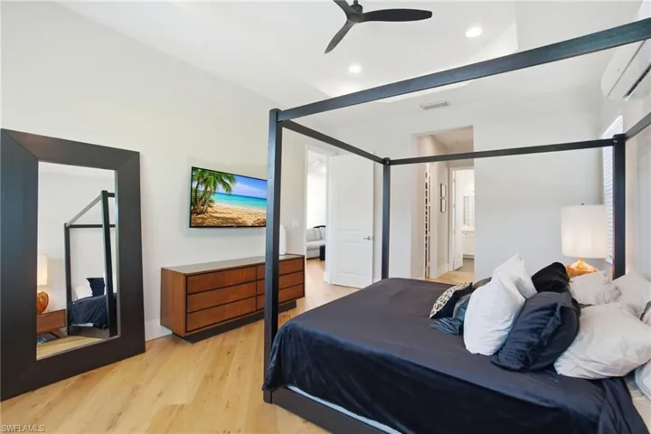 Bedroom featuring light wood-style flooring, an AC wall unit, a ceiling fan, and connected bathroom