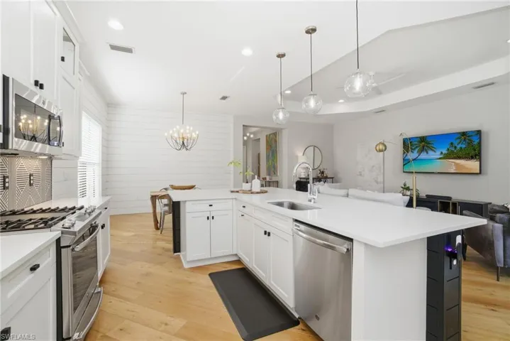 Kitchen featuring white cabinetry, stainless steel appliances, light wood-style flooring, an island with sink, and wood walls