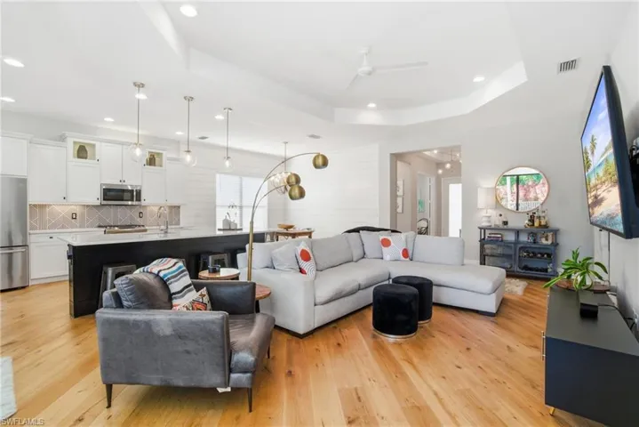 Living room with ceiling fan, light wood-type flooring, a tray ceiling, and recessed lighting