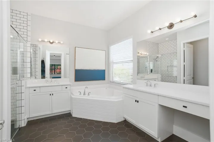 Bathroom with a garden tub, two vanities, dark tile patterned flooring, and a shower stall