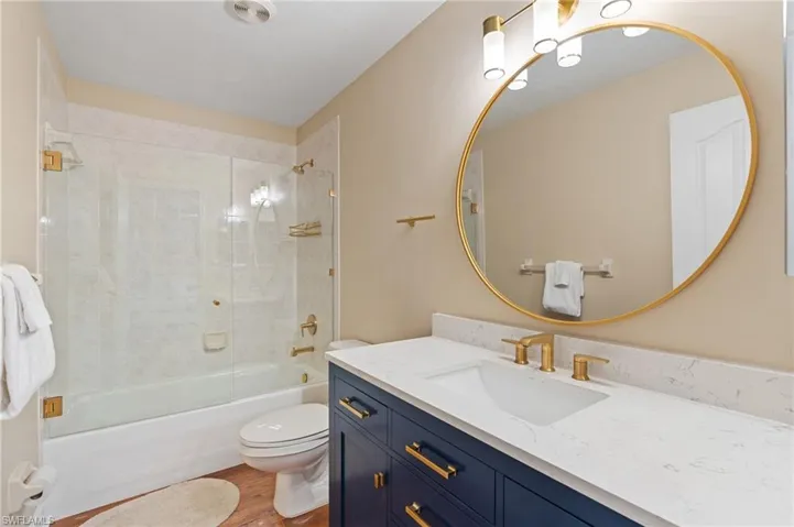 Full bathroom with vanity, hardwood / wood-style flooring, toilet, and enclosed tub / shower combo