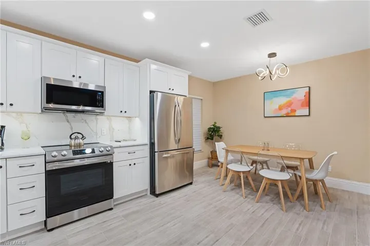Kitchen with appliances with stainless steel finishes, an inviting chandelier, tasteful backsplash, and white cabinetry