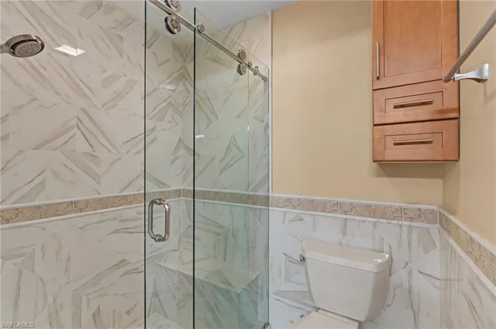 Bathroom featuring toilet, a shower with door, and tile walls