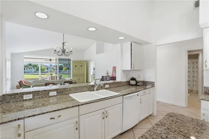 Kitchen with a double basin sink, light-toned granite countertops, and white cabinetry