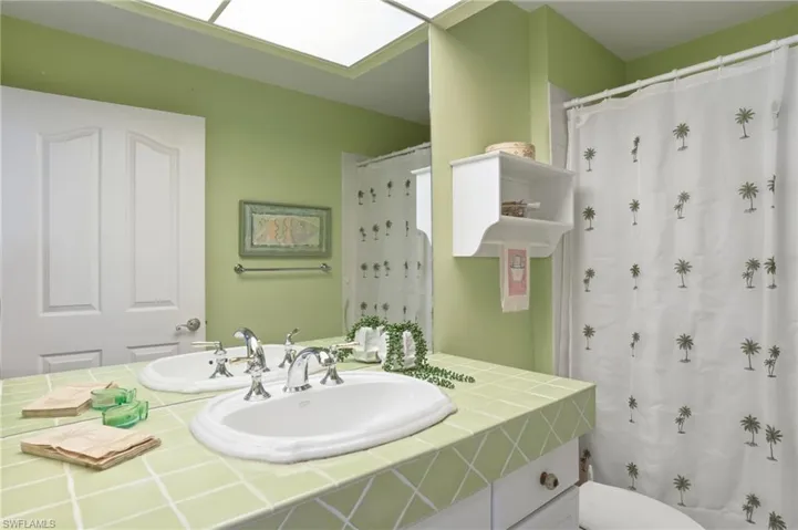 Bathroom featuring a dual vanity with undermount sinks, light green tiled countertop, and chrome fixtures