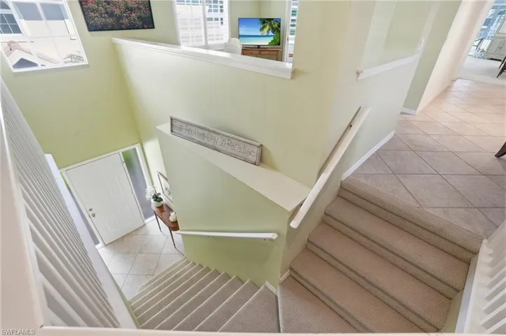 Multi-level interior featuring a carpeted staircase with white railings, tile flooring at the entry, and a white paneled entry door