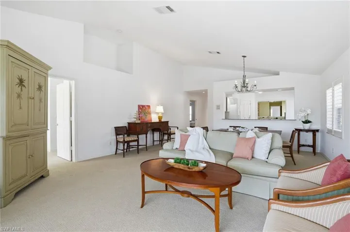 Spacious living area featuring vaulted ceilings, neutral carpeting, and a pass-through window to the kitchen