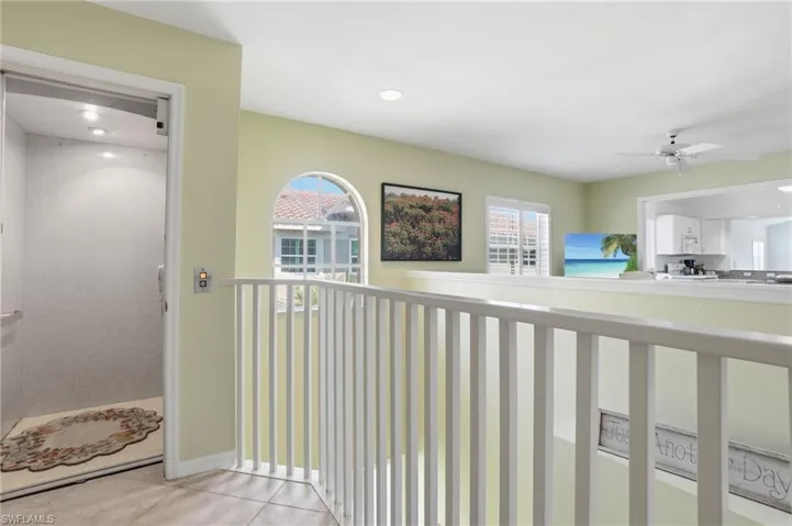 Upper-level hallway featuring a built-in elevator, arched window, and white railing