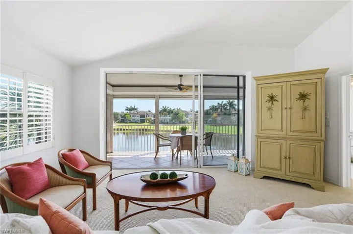 Living area featuring vaulted ceilings, light-hued carpeting, plantation shutters, and sliding glass doors opening to a screened balcony overlooking a water feature