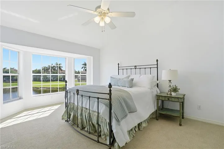 Room featuring a bay window overlooking a lake, carpeted flooring, a ceiling fan, and white walls