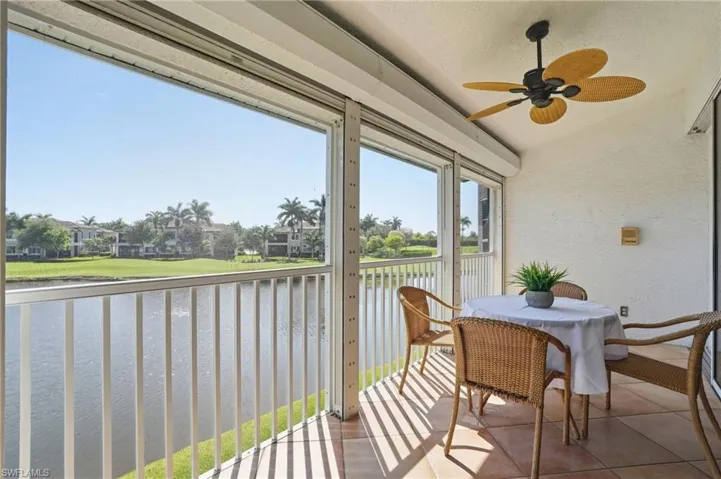 Screened balcony featuring a ceiling fan, terracotta-toned tile flooring, and a white railing overlooking a body of water with distant structures