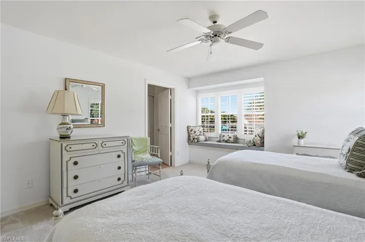 Bright bedroom featuring a built-in window seat, plantation shutters, and a ceiling fan